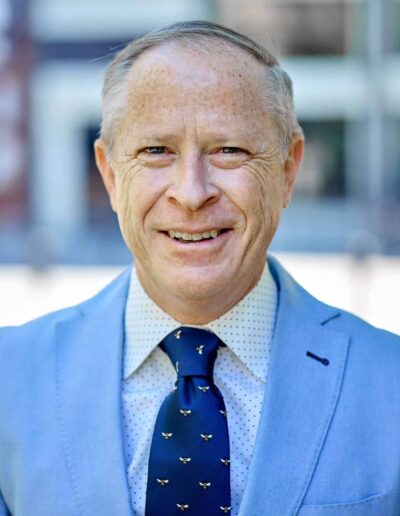 Smiling man in a light blue suit and navy tie outdoors.