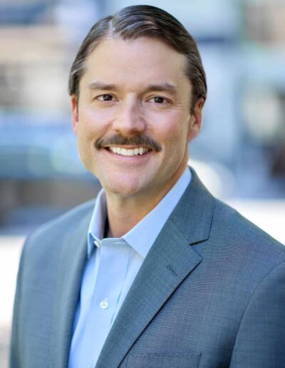 Smiling man in a blue suit outdoors, portrait-style headshot.